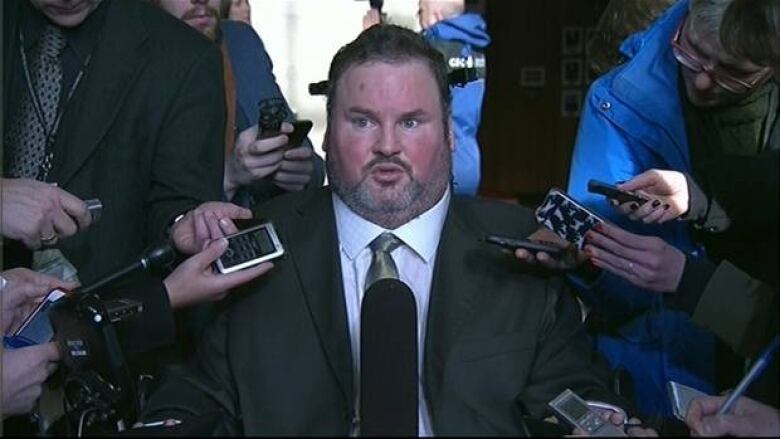 A man in a wheelchair faces reporters with microphones in their hands.