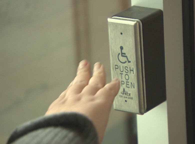 a person's hand  reaches toward a push to open button at a doorway