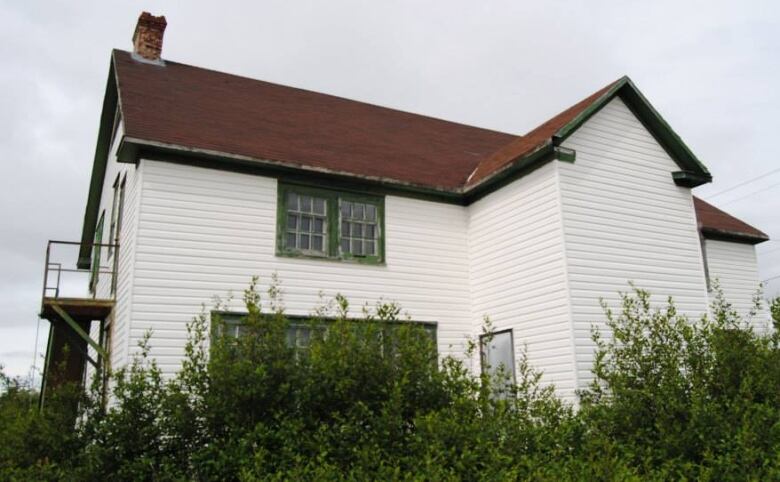 An old white building with green trim on the windows. 