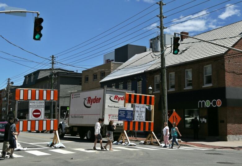 Road signs that say Road Closed are clustered at any intersection in front of businesses. A large Ryder truck is parked behind the signs.