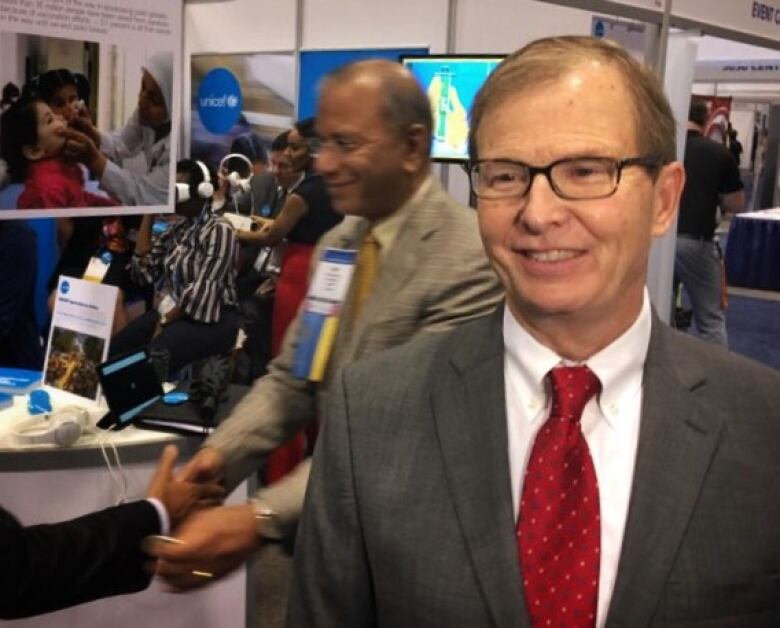 A middle-aged man in a grey suit, red tie and glasses poses for a picture.