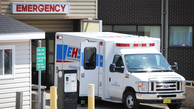 An ambulance is backed up to the door of a brick building with a sign saying 