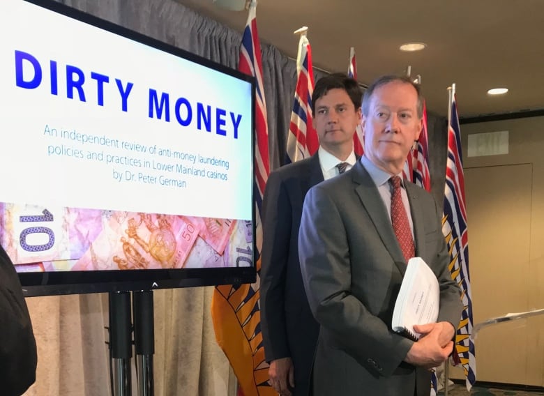 Two men are pictured at a news conference, in front of a screen that reads 'Dirty Money'.