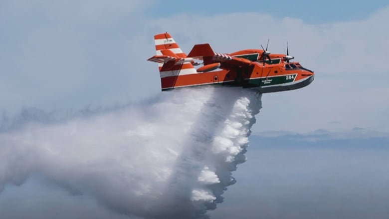 An orange aircraft releases water below it.