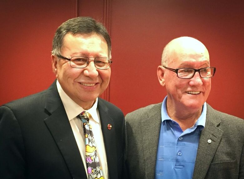 Two men with glasses stand side by side and smile.