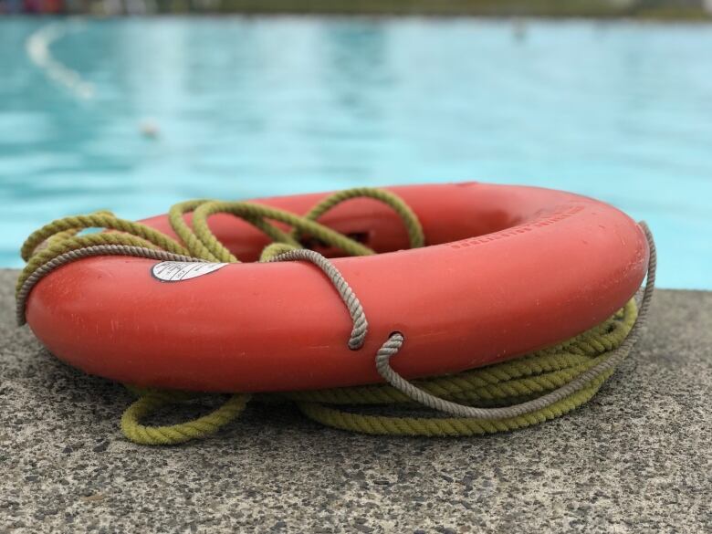 A red lifeguard flotation device ring is pictured at the edge of a pool.