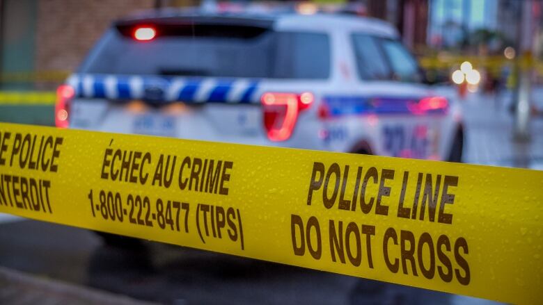 A blue and white police vehicle behind yellow crime tape on a rainy day.