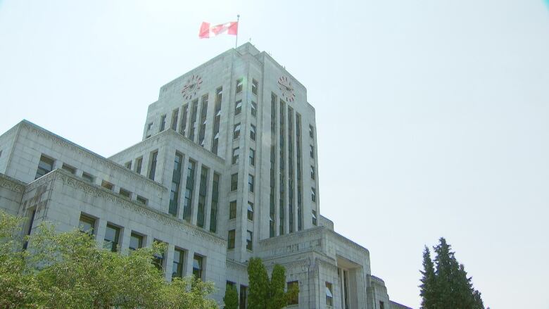 Vancouver City Hall, complex of buildings including a tall, central building with a clock and Canadian flag at the top, is pictured in the day time.