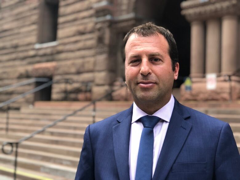 A man in a blue suit and tie stands outside a courthouse.