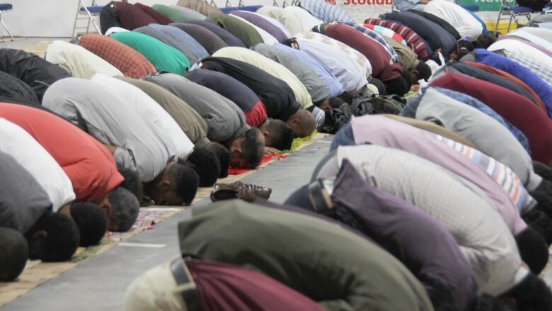 Men kneel and bend their heads to the floor in prayer