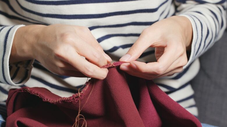 Hands belonging to someone in a striped shirt stitch a red garment.