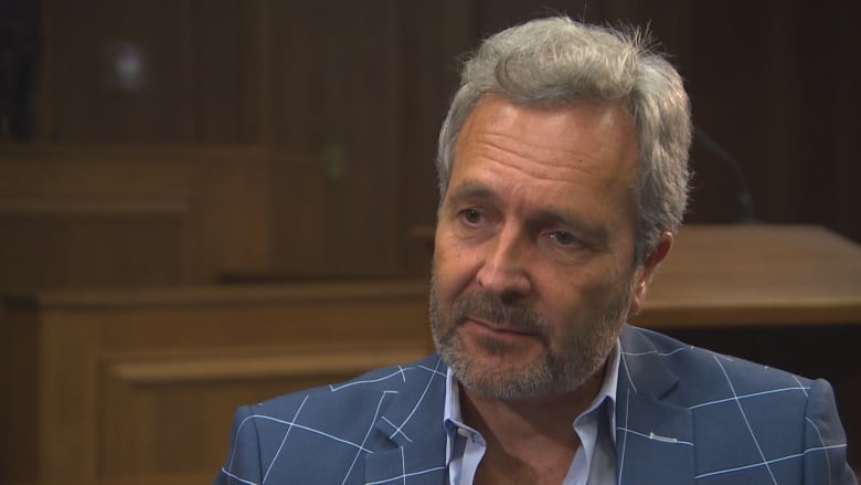 Manitoba Court of King's Bench Chief Justice Glenn Joyal sits in a room with wooden walls in the background. He's wearing a blue suit with white stripes.