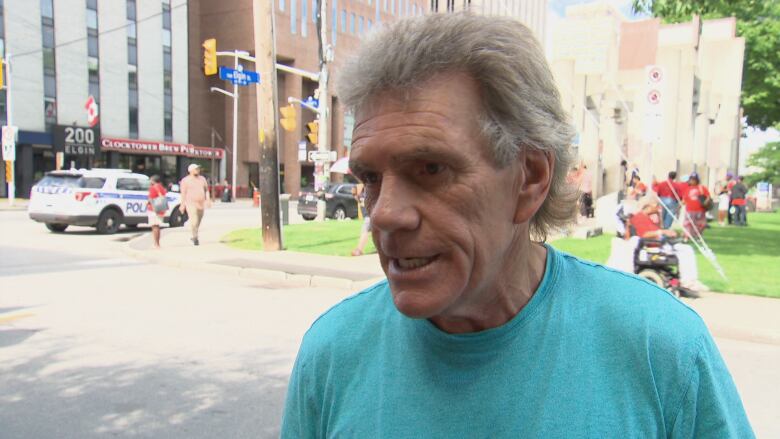 A man in a teal shirt stands outside on a sunny day.