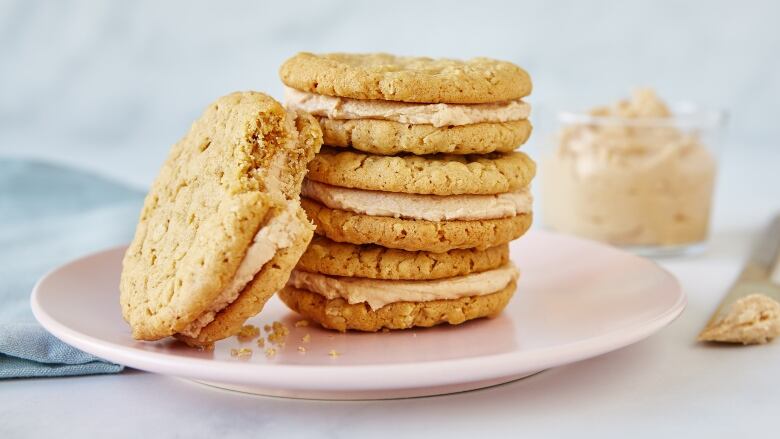 A stack of Peanut Butter Sandwich Cookies filled with peanut butter buttercream icing. They're sitting on a light pink plate. 