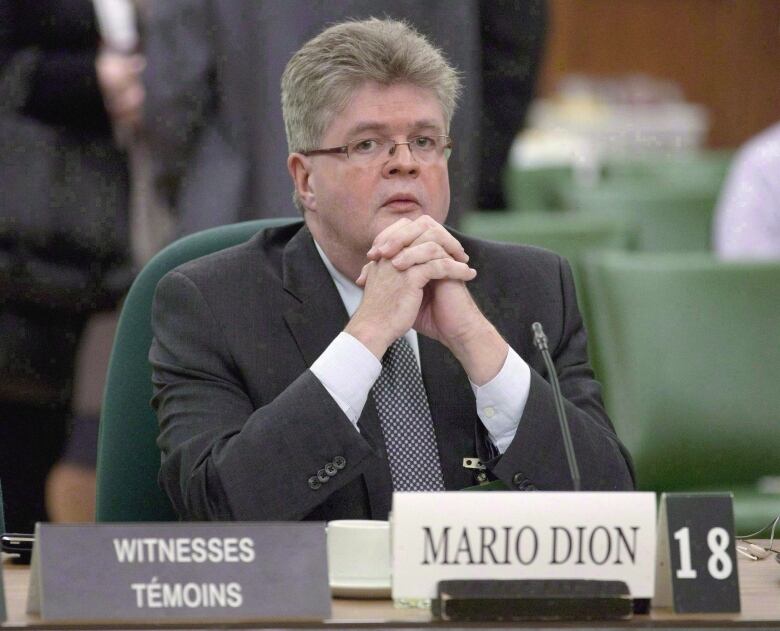 A man in a suit sits with his hands held under his chin. 