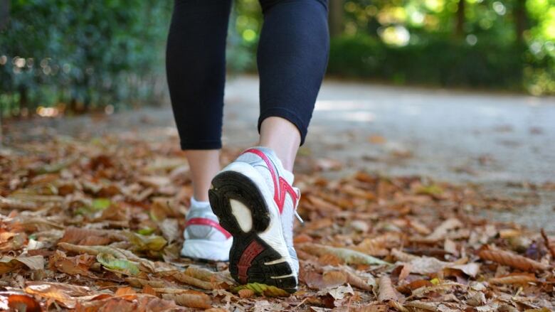 A woman's lower legs and feet are seen wearing leggings and running shoes and walking down a street where leaves have fallen.