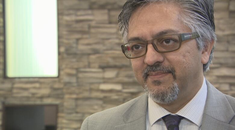 A man in glasses looks at the camera. He's in a suit, with pepper-grey hair.