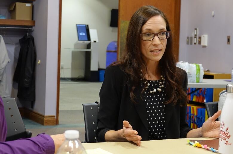 A woman seated at a table in an office speaks while a man listens.