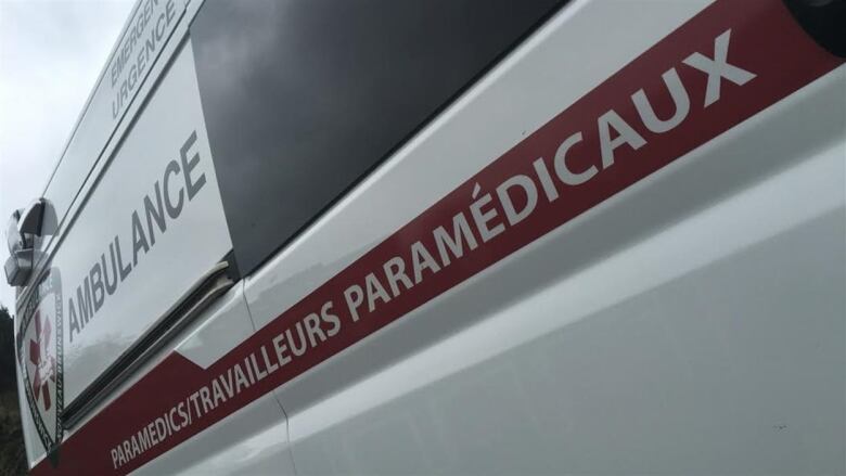 A photo of a white ambulance taken of the side of the vehcile, with a dark red stripe on it that says paramedics.