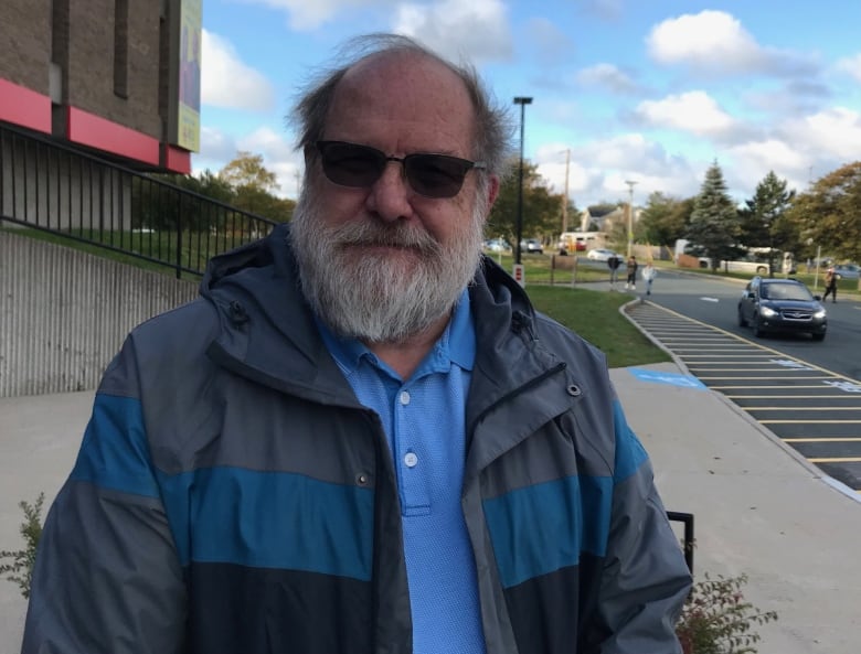 A smiling man with a grey beard and sunglasses sits outside the CBC studio in St. John's.