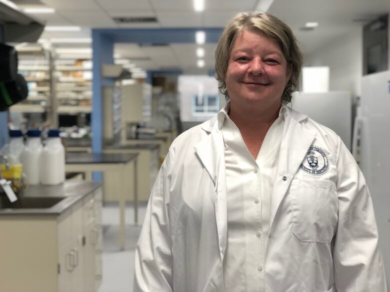 Woman wearing white lab coat, smiling.