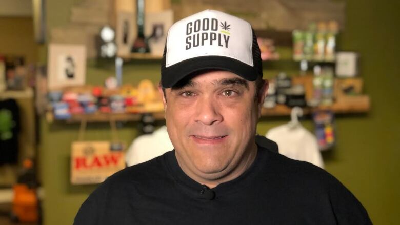 A man wearing a black hat and black t shirt standing inside a cannabis supply store. 