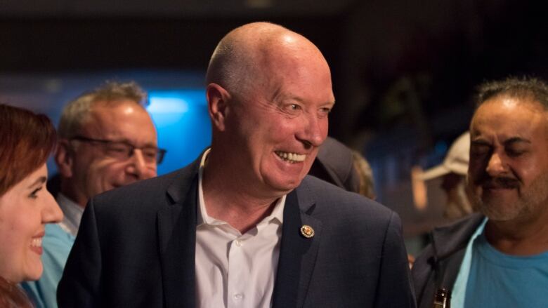 Burnaby mayor Mike Hurley smiles at someone off-camera. There are people smiling in the background.