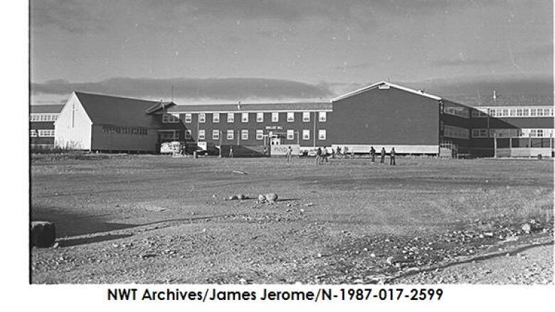 Black and white photo of a large two-story building on a very flat landscape.