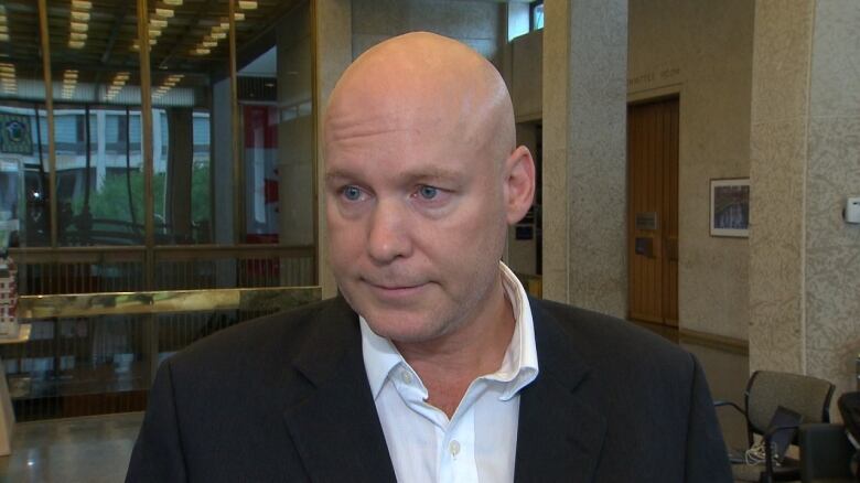 A man wearing a white dress shirt and black jacket stands in city hall.