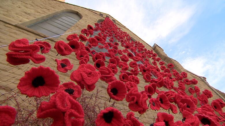 A photo shot from below of knit poppies against a brick building. 