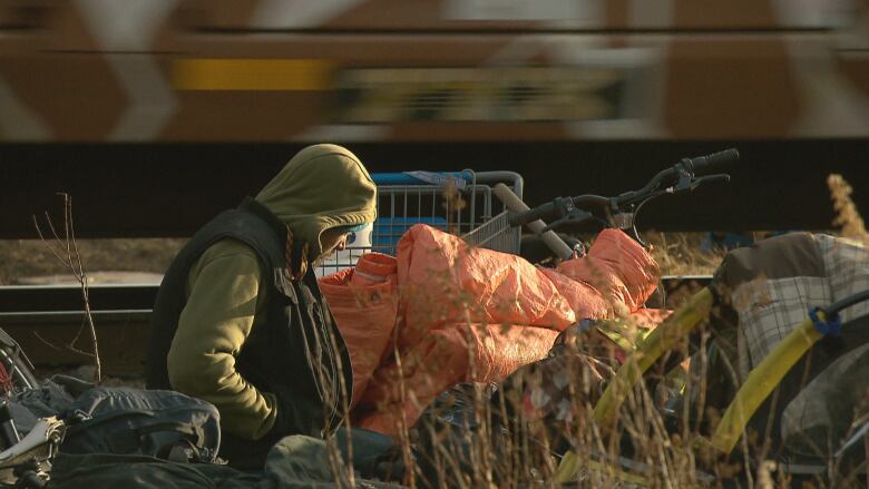 A person with their hood up next to a bicycle piled with orange bags