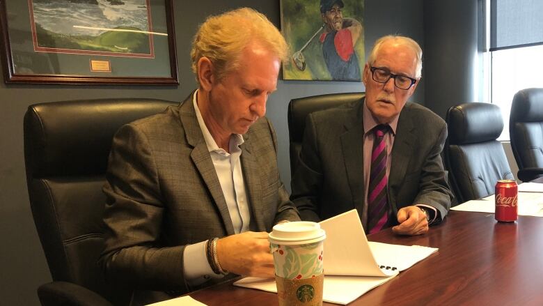 Two men in suits at a boardroom table.