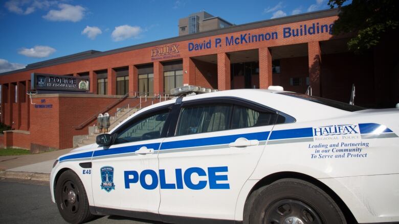 A police cruiser sits outside of a low, brick building bearing the words 