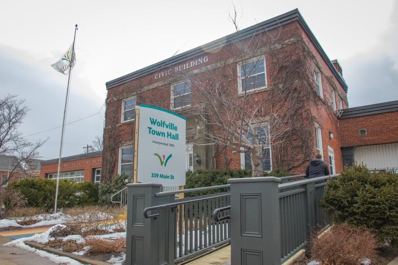 A two-storey brick building is covered with bare ivy branches, while a town sign and flagpole stand outside the hall