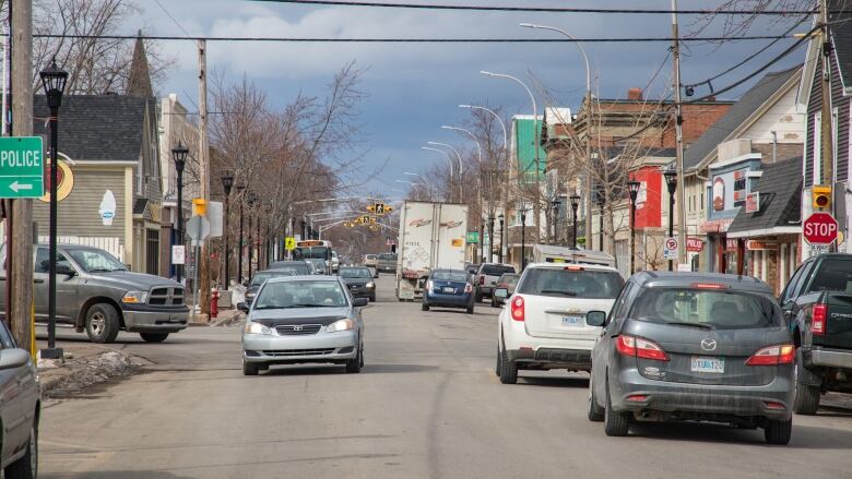 Cars drive down a street with shops and homes on either side