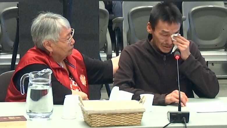 A man cries sitting at a table next to a woman 