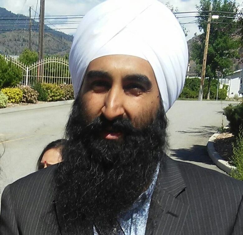 A profile photo of a middle aged Sikh man with a brown beard  wearing a white turban