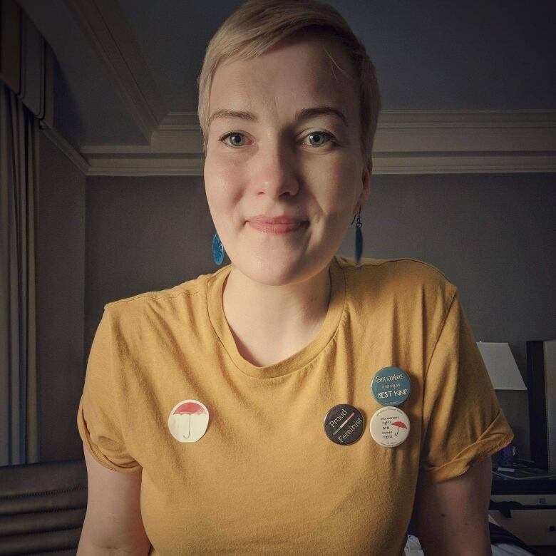 A self-portrait of a woman in a yellow shirt with pins on it.