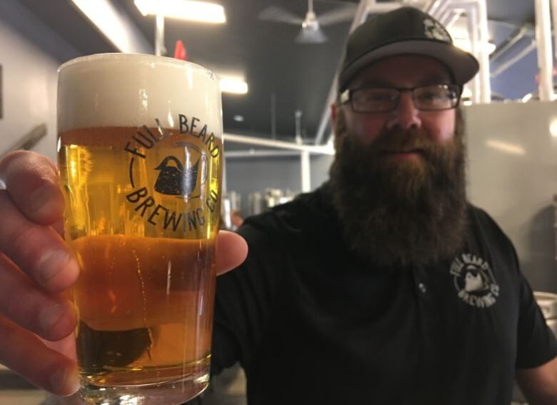 A man with a beard holding a glass of beer.