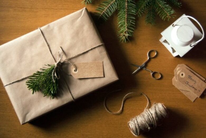 A package wrapped in plain brown paper and cotton string with a sprig of spruce tree tied on as a decoration. 