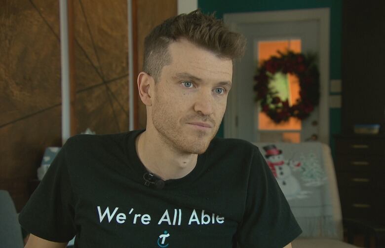 A man with short brown hair and a black t-shirt that says 