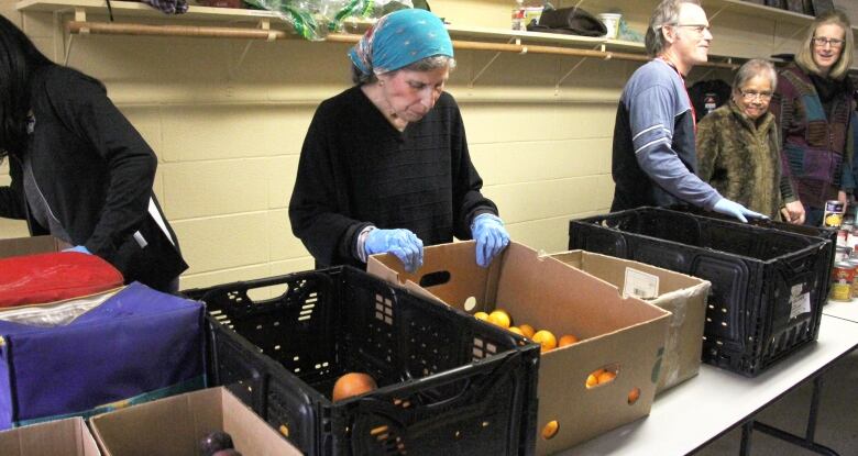 A person stands behind a table. On the table are cardboard boxes with oranges and plums and a crate of grapefruit.