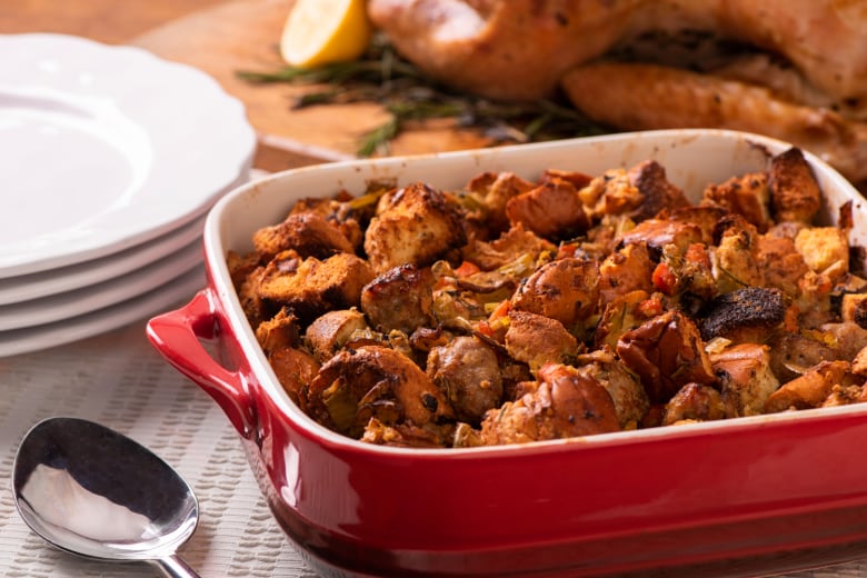 A red casserole pan filled with Brioche and Sausage Stuffing Bake sitting on a table. 