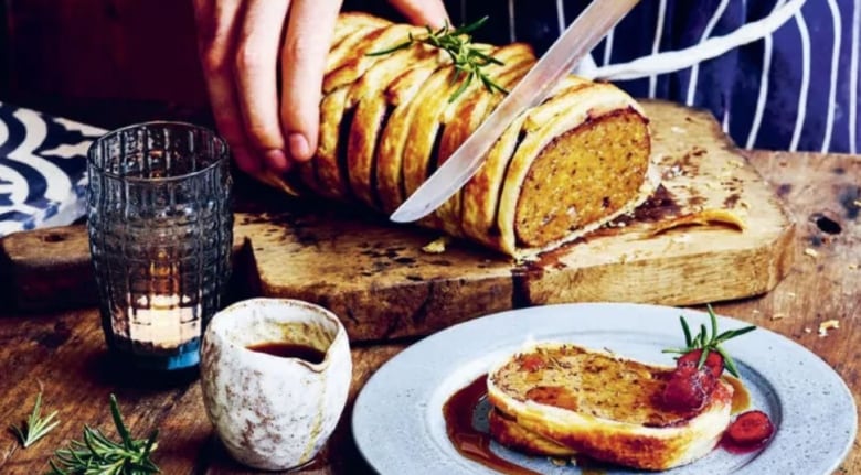 Hands slicing a meatless roast on a wooden cutting board. 