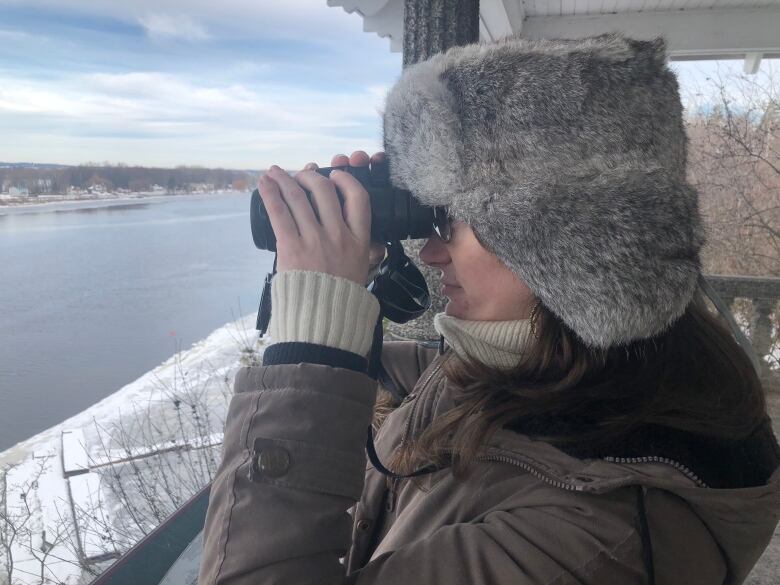 Someone looks over a river in winter using binoculars.