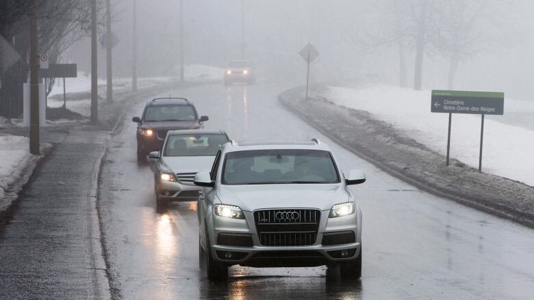 Two SUVs and a sedan are seen driving down a paved street in the rain