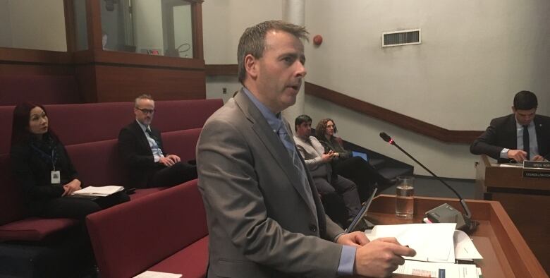 Man pictured from side wearing suit speaking at podium