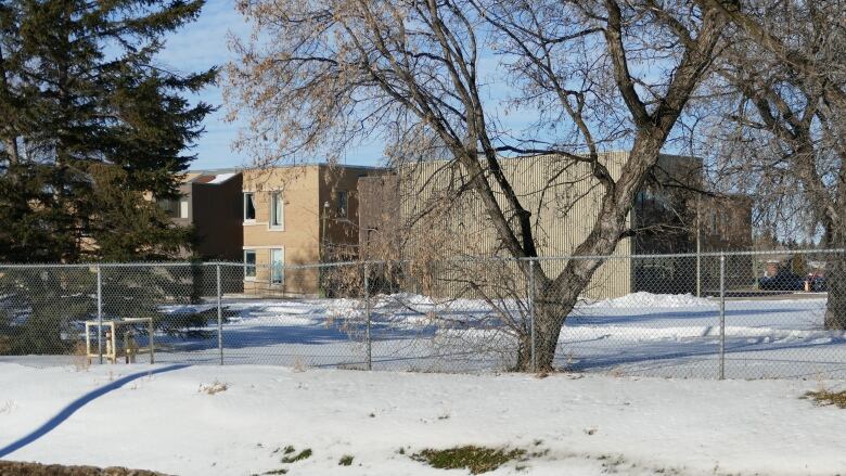 A building sits in grounds behind a chain-link fence.