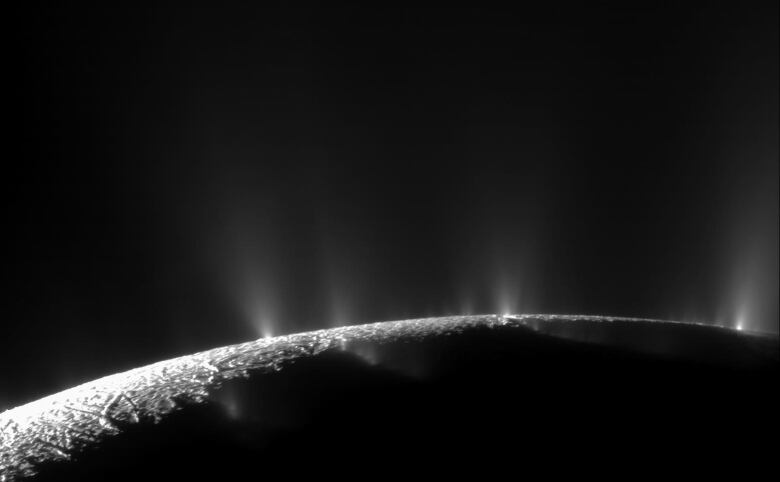 We see a black and white image taken at the surface of Saturn's moon Enceladus. The moon's rough icy surface has bright jets of water shooting out into space. 