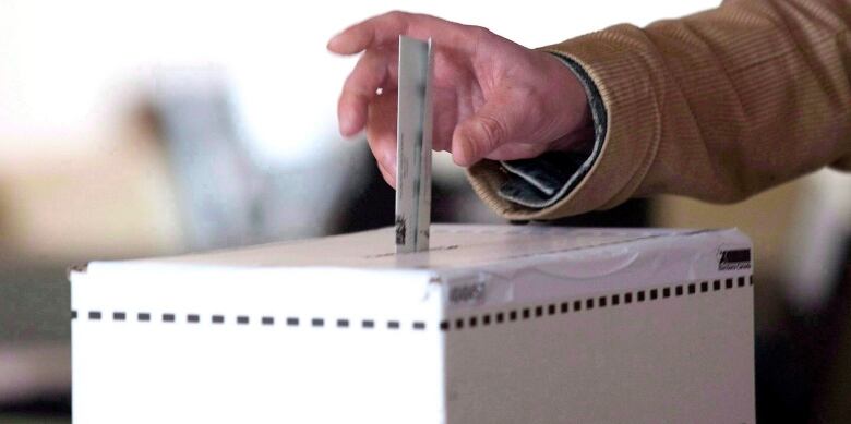 A hand places a ballot into a ballot box.